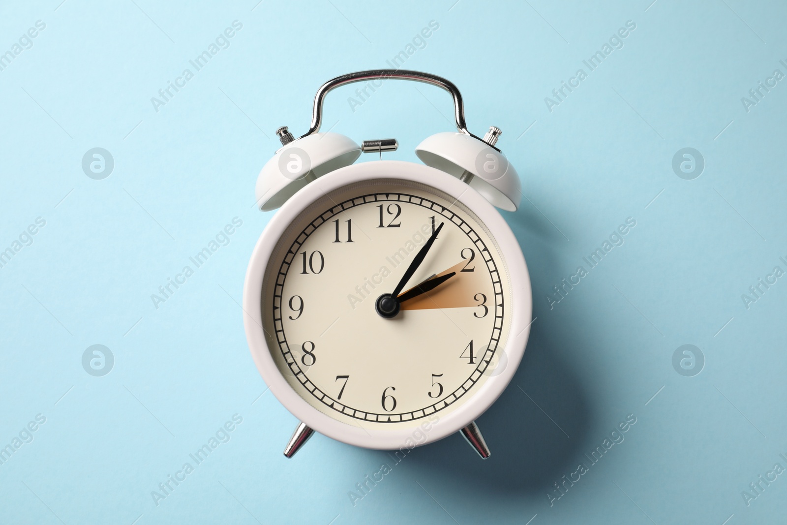 Image of Daylight saving time. White alarm clock on light blue background, top view. Highlighted area showing time change by one hour forward