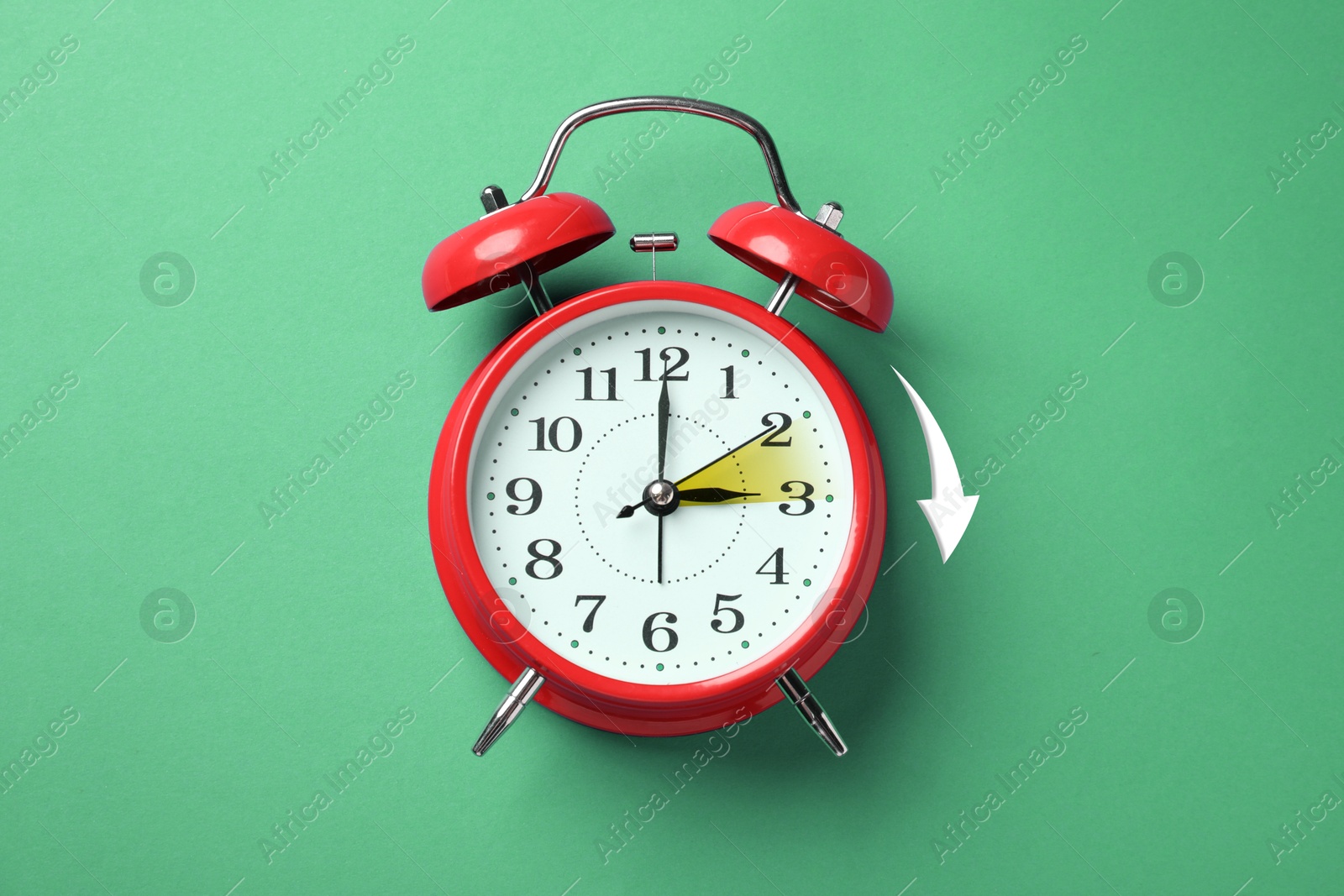 Image of Daylight saving time. Red alarm clock on green background, top view. Highlighted area and arrow showing time change by one hour forward