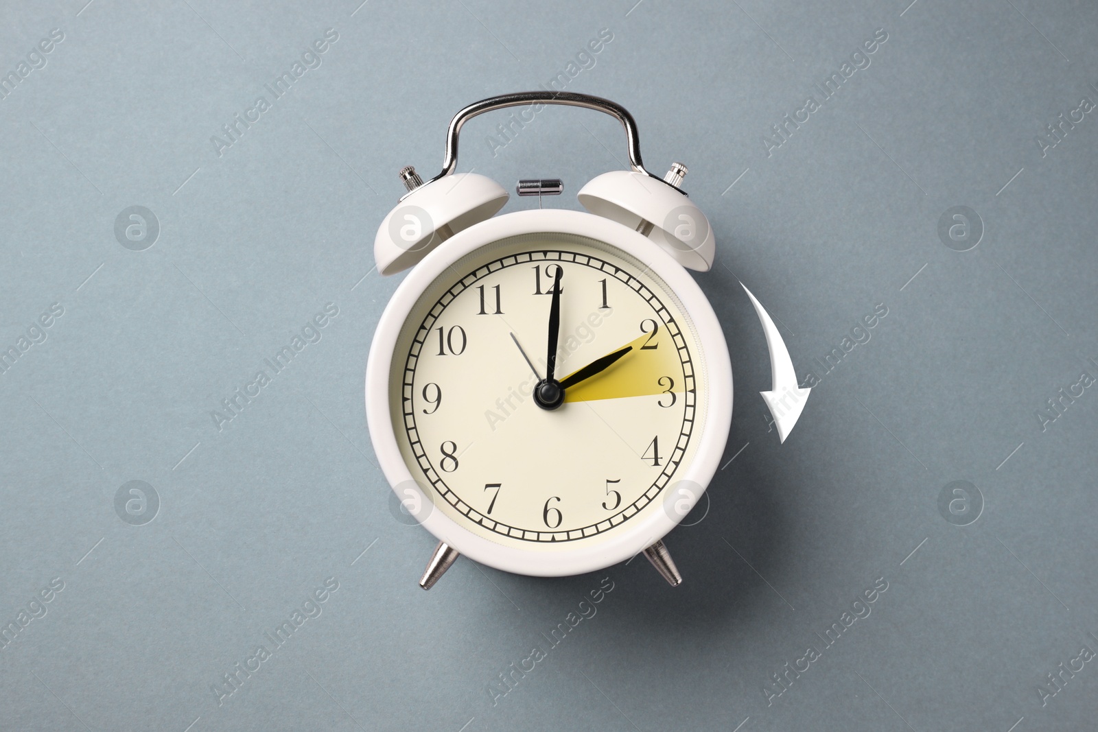 Image of Daylight saving time. White alarm clock on grey background, top view. Highlighted area and arrow showing time change by one hour forward