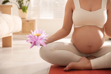 Image of Pregnant woman meditating with beautiful lotus flower in her hand at home, closeup. Padmasana (yoga lotus position)