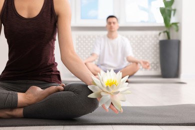 Image of Woman meditating with beautiful lotus flower in her hand indoors. Padmasana (yoga lotus position)