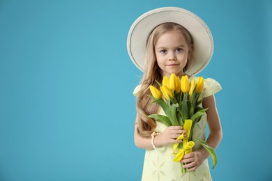 Cute little girl with beautiful yellow tulips on light blue background, space for text. Spring season