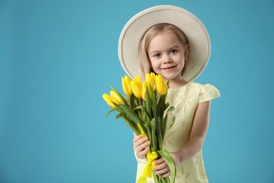 Photo of Cute little girl with beautiful yellow tulips on light blue background, space for text. Spring season