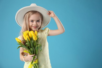 Cute little girl with beautiful yellow tulips on light blue background, space for text. Spring season