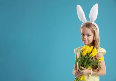 Cute little girl with bunny ears and tulips on light blue background, space for text. Easter celebration