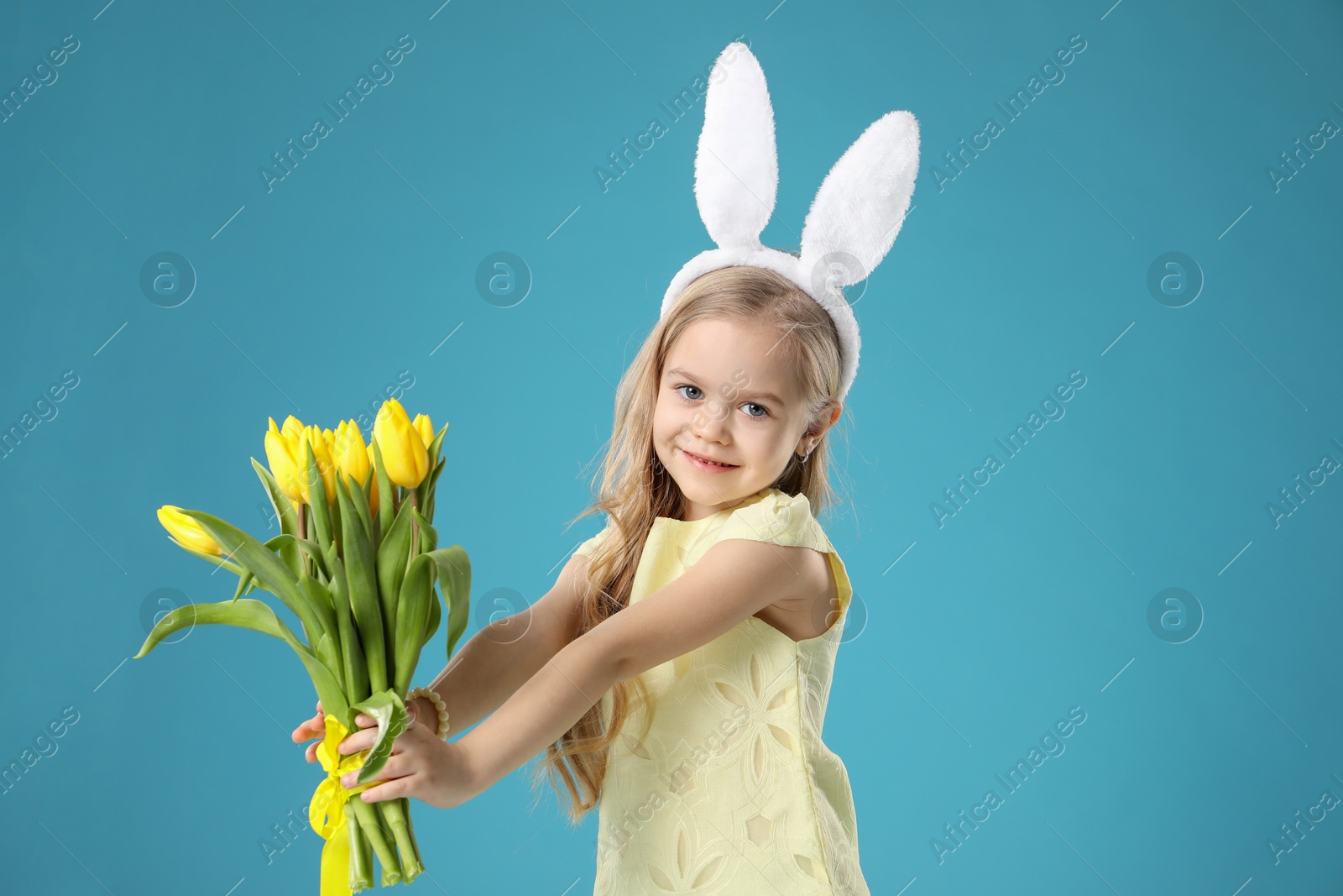 Photo of Cute little girl with bunny ears and tulips on light blue background. Easter celebration