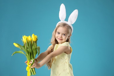 Photo of Cute little girl with bunny ears and tulips on light blue background. Easter celebration