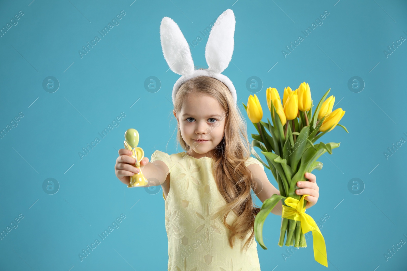 Photo of Cute little girl with bunny ears and tulips on light blue background. Easter celebration