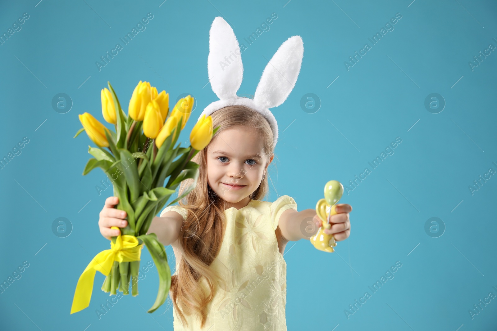 Photo of Cute little girl with bunny ears and tulips on light blue background. Easter celebration