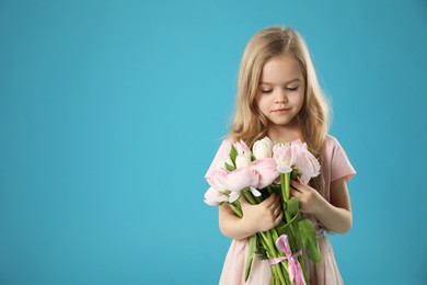 Photo of Cute little girl with bouquet of beautiful spring flowers on light blue background, space for text