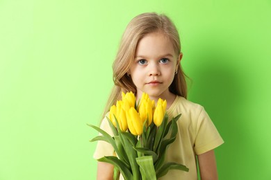 Cute little girl with beautiful yellow tulips on green background. Spring season