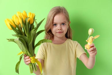 Photo of Cute little girl with yellow tulips and decorative bunny on green background. Easter celebration