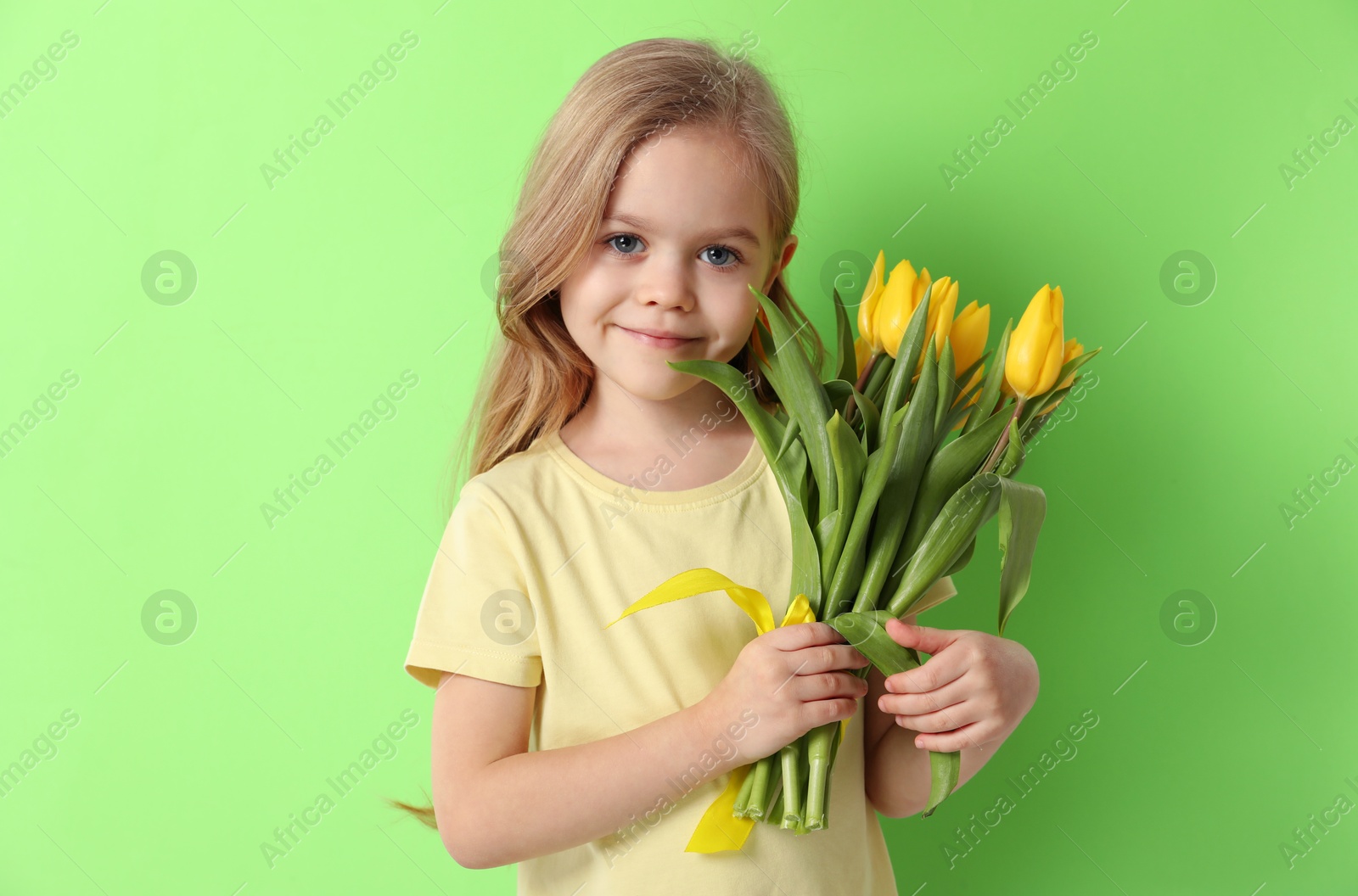 Photo of Cute little girl with beautiful yellow tulips on green background. Spring season