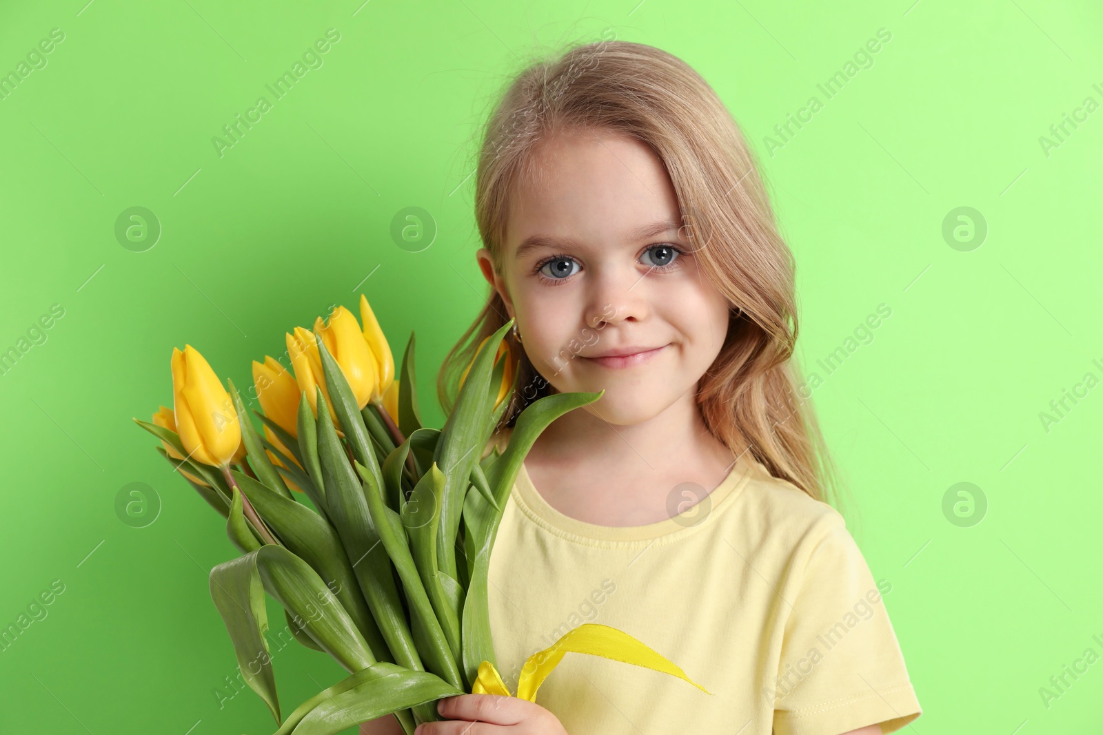 Photo of Cute little girl with beautiful yellow tulips on green background. Spring season