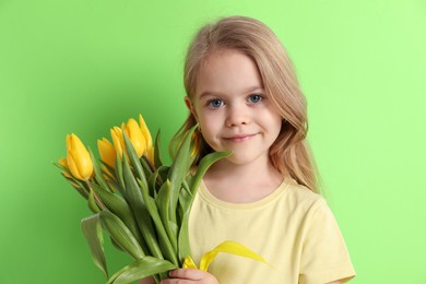 Photo of Cute little girl with beautiful yellow tulips on green background. Spring season