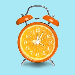 Image of Alarm clock with sliced orange instead of dial on light blue background