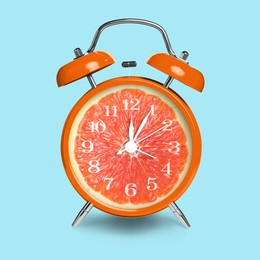 Image of Alarm clock with sliced orange instead of dial on light blue background