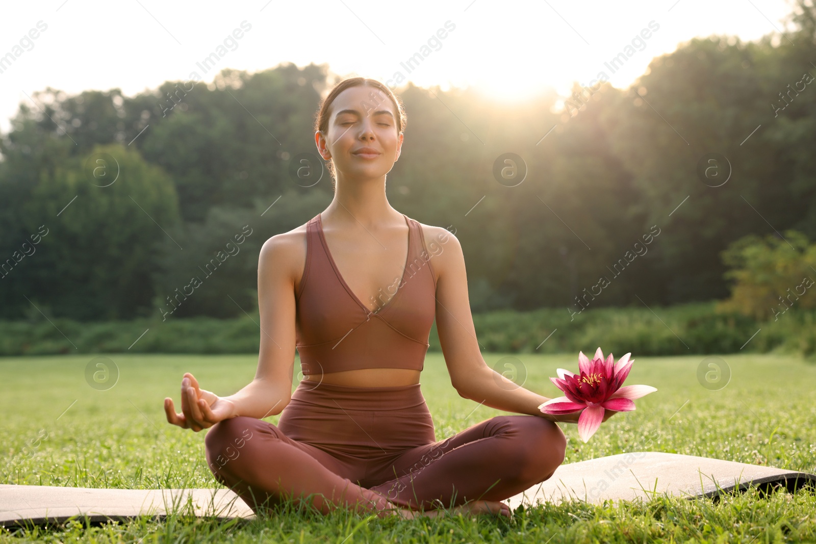 Image of Woman meditating with beautiful lotus flower in her hand outdoors on sunny morning. Padmasana (yoga lotus position)