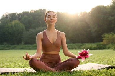 Image of Woman meditating with beautiful lotus flower in her hand outdoors on sunny morning. Padmasana (yoga lotus position)