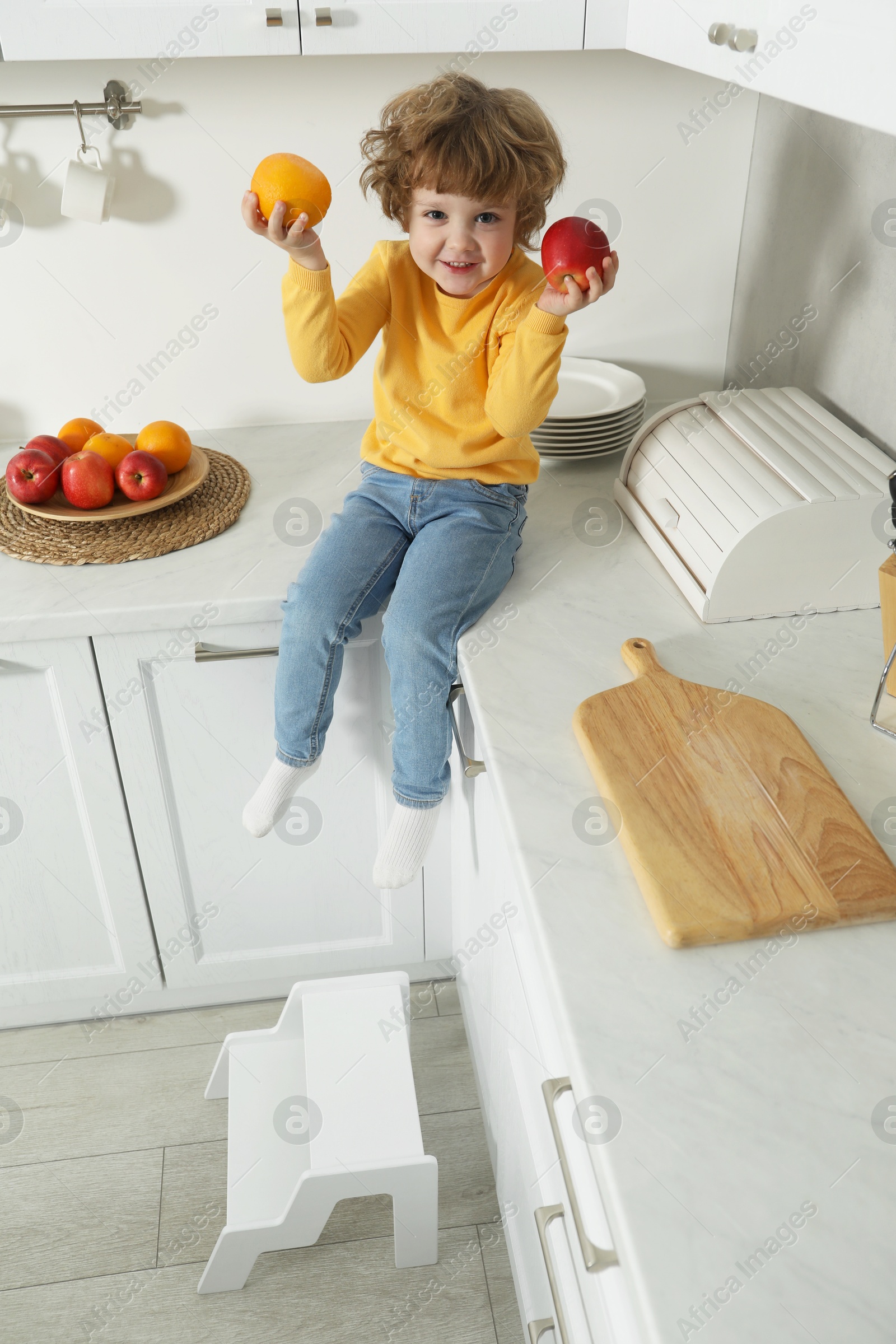 Photo of Little boy with fruits on countertop and step stool in kitchen