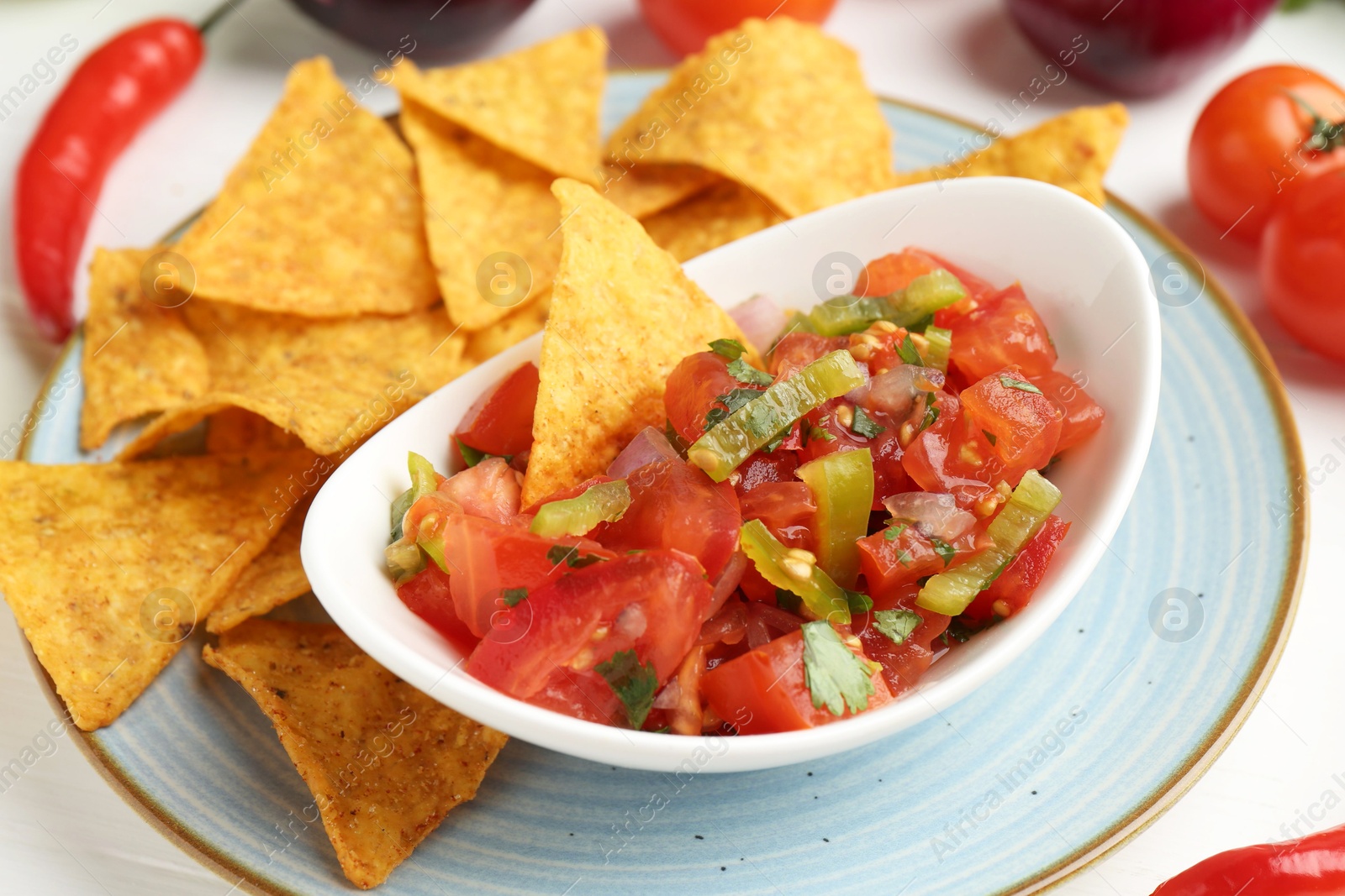 Photo of Delicious salsa (Pico de gallo) served with nachos and products on white table, closeup