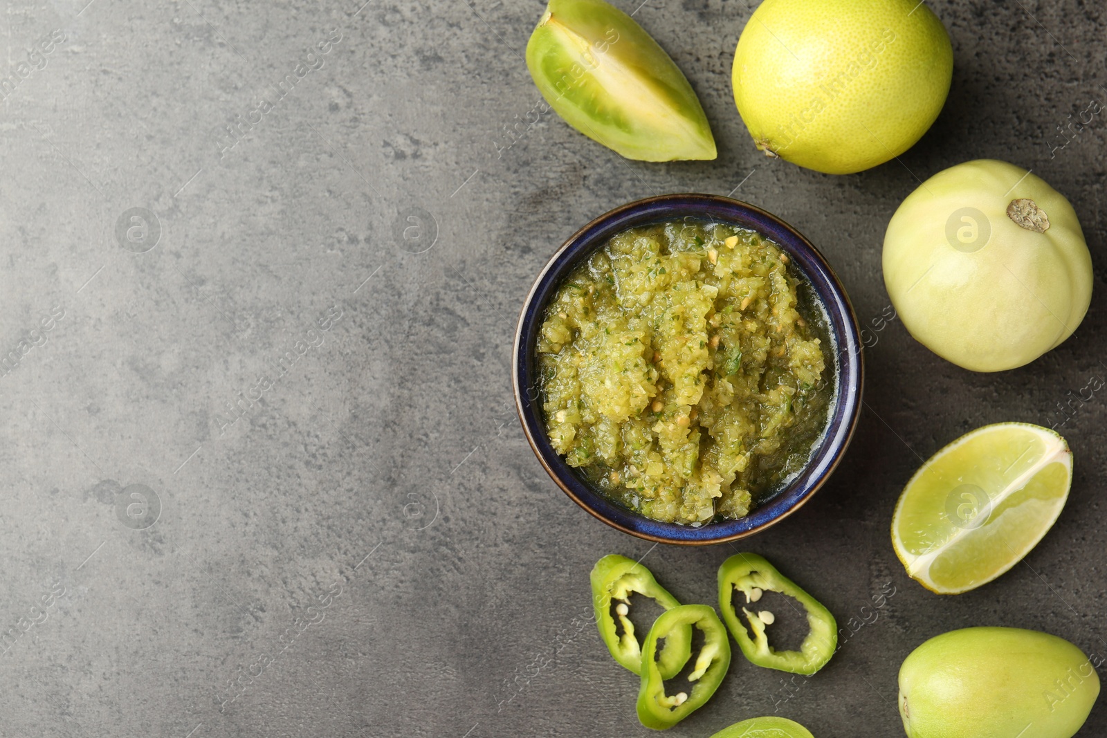 Photo of Delicious salsa sauce in bowl and products on grey textured table, flat lay. Space for text