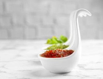 Photo of Sauce boats with salsa on white marble table, selective focus. Space for text