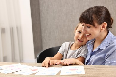 Smiling speech therapist working with little girl at table in autism treatment center. Space for text