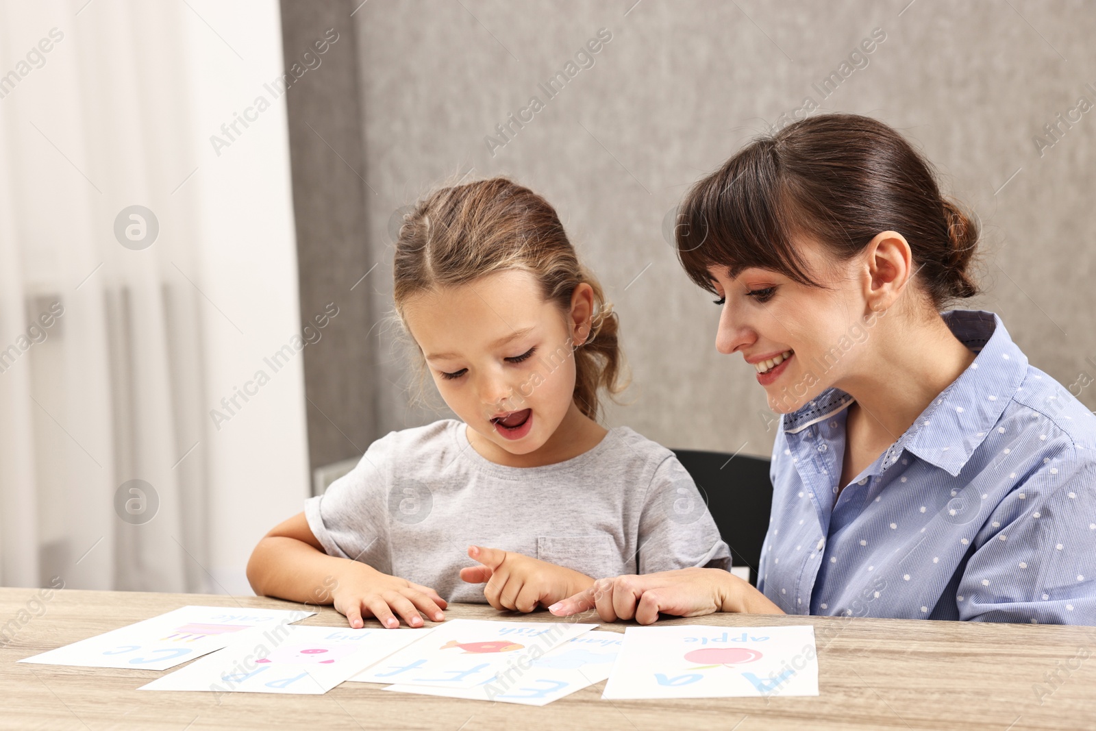 Photo of Smiling speech therapist working with little girl at table in autism treatment center