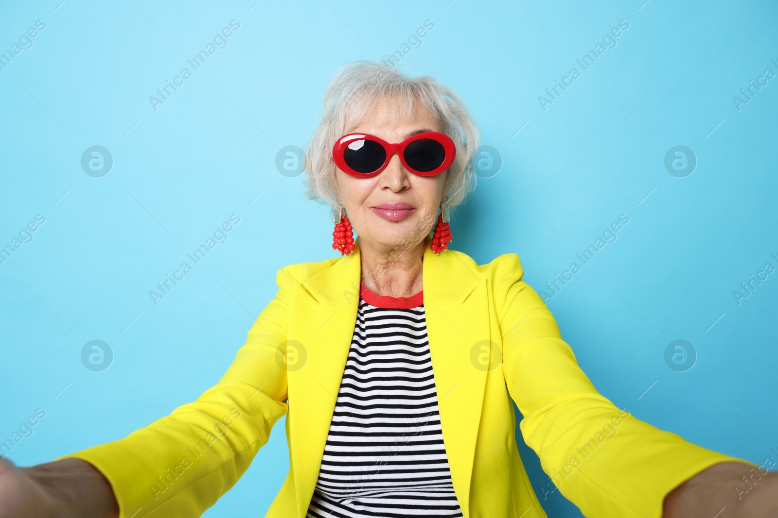 Photo of Fashionable grandmother taking selfie on light blue background