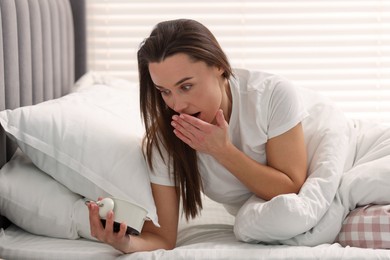 Overslept woman with alarm clock in bed at home