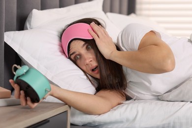 Overslept woman with alarm clock in bed at home