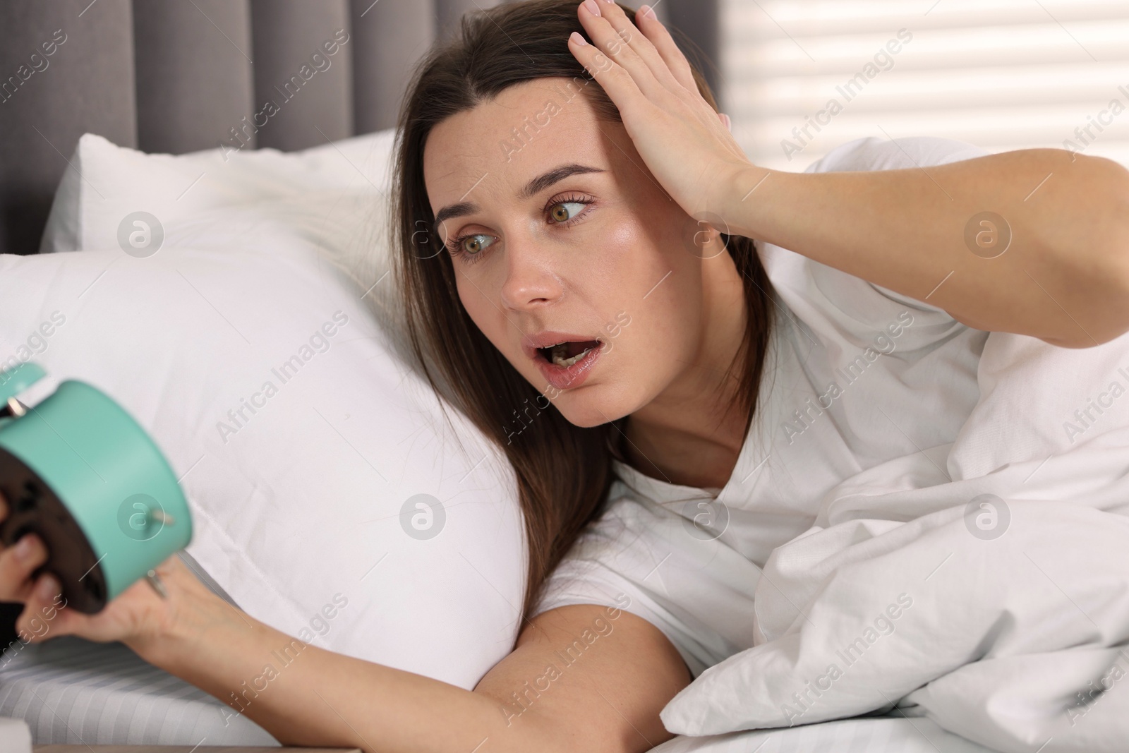 Photo of Overslept woman with alarm clock in bed at home