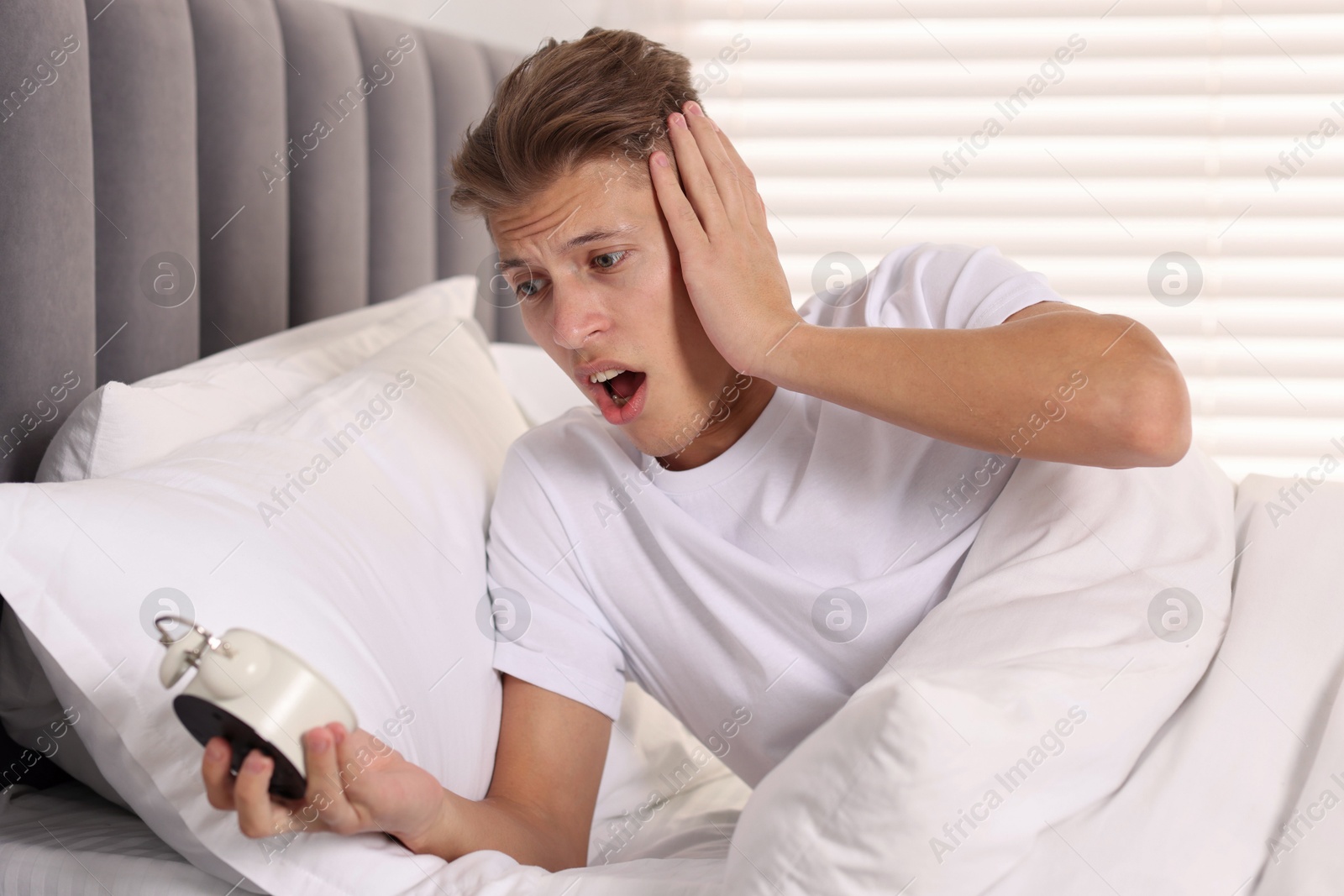 Photo of Overslept man with alarm clock in bed at home