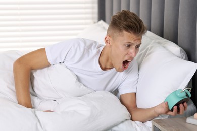 Overslept man with alarm clock in bed at home