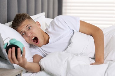 Overslept man with alarm clock in bed at home