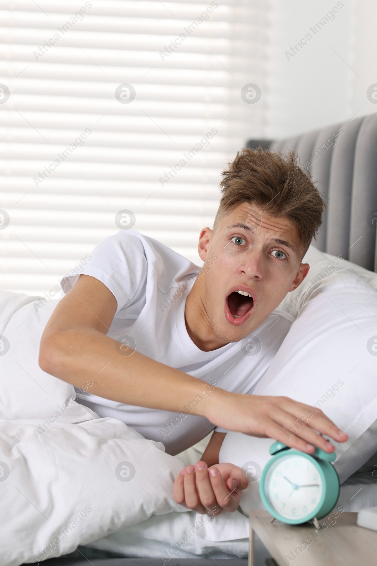 Photo of Overslept man with alarm clock in bed at home