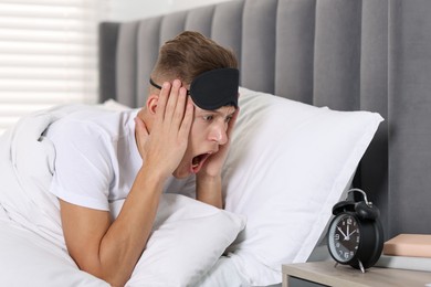 Overslept man with alarm clock in bed at home