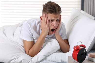 Photo of Overslept man with alarm clock in bed at home