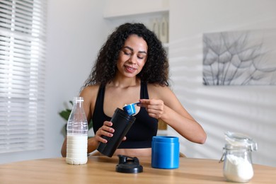 Photo of Beautiful woman making protein shake at wooden table indoors