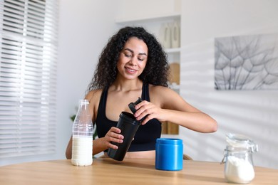 Photo of Beautiful woman making protein shake at wooden table indoors