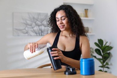 Photo of Beautiful woman making protein shake at wooden table indoors