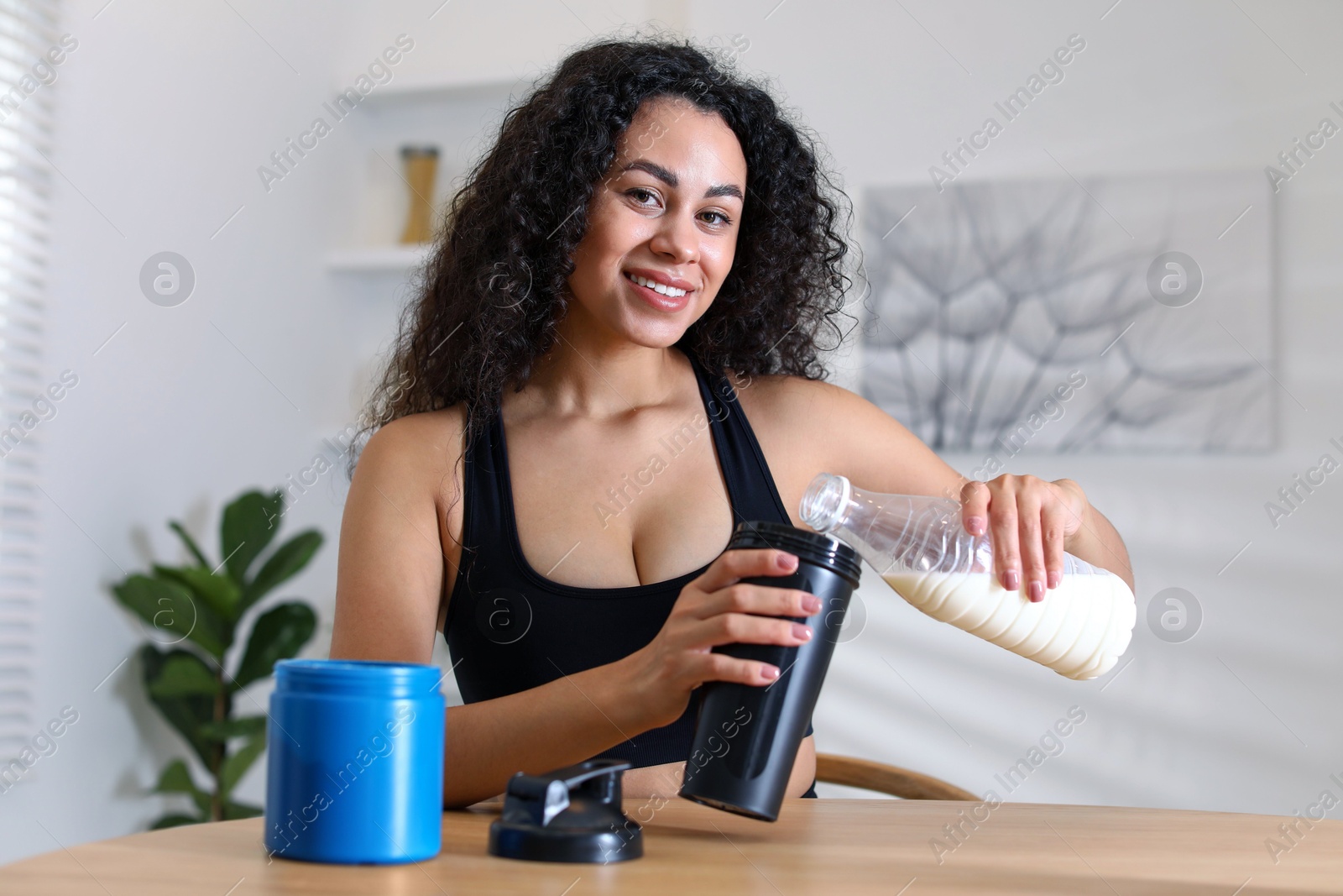 Photo of Beautiful woman making protein shake at wooden table indoors