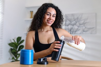 Photo of Beautiful woman making protein shake at wooden table indoors