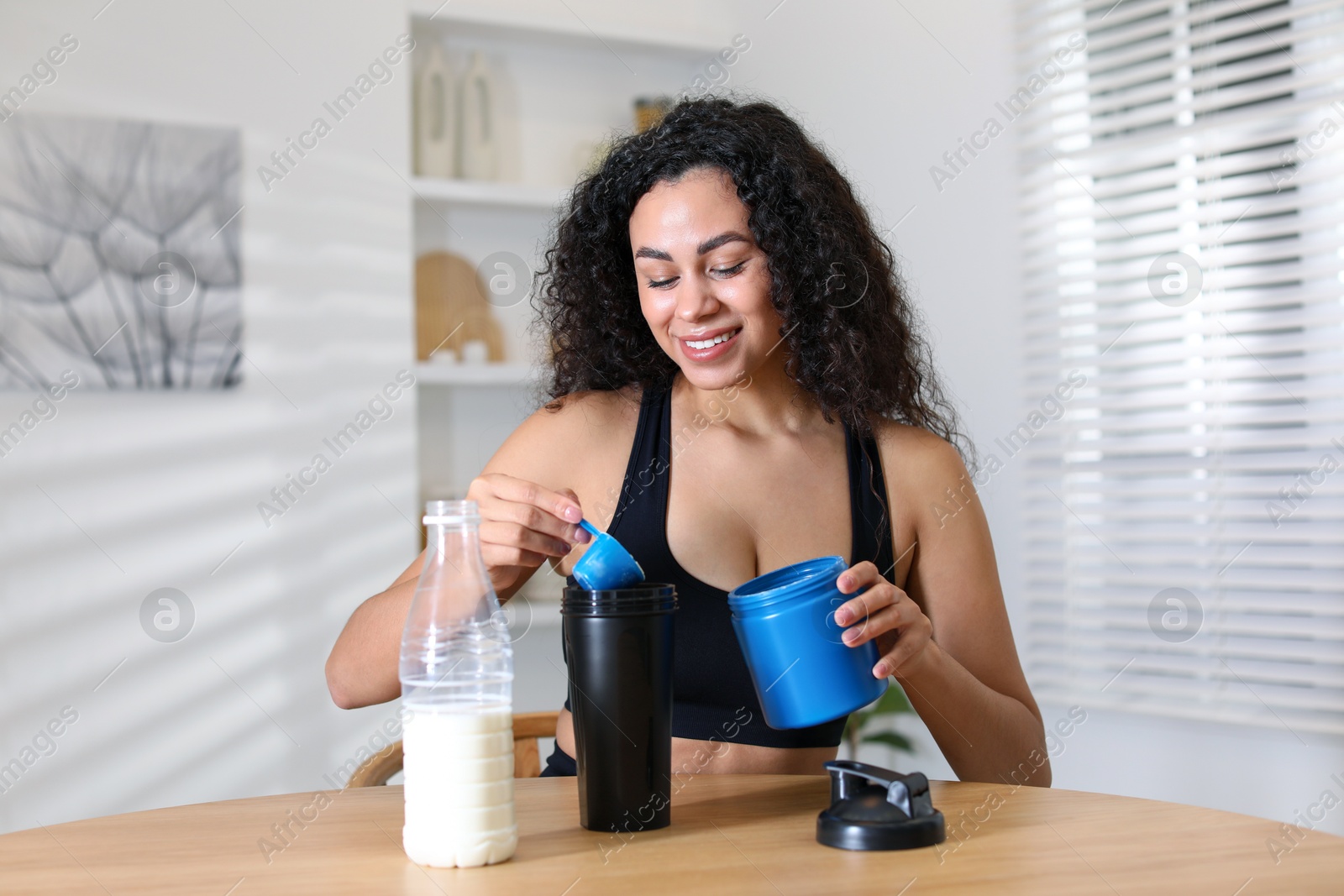 Photo of Beautiful woman making protein shake at wooden table indoors