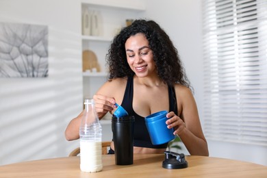 Beautiful woman making protein shake at wooden table indoors