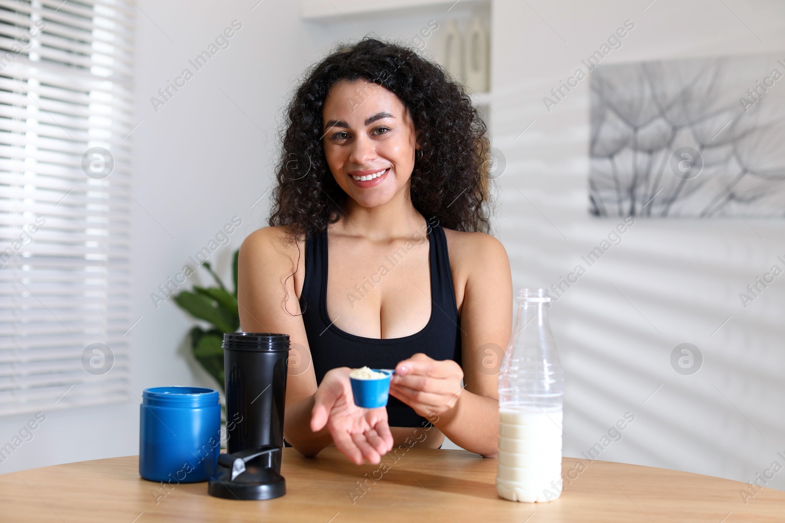 Photo of Beautiful woman making protein shake at wooden table indoors