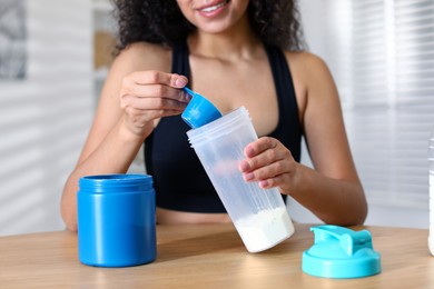 Beautiful woman making protein shake at wooden table indoors, closeup