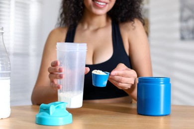 Photo of Beautiful woman making protein shake at wooden table indoors, closeup