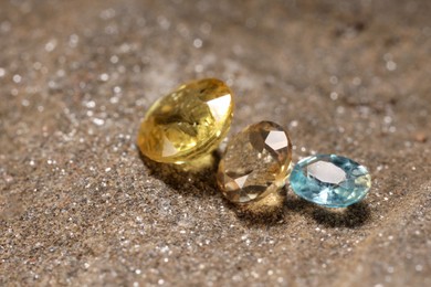 Photo of Beautiful shiny gemstones on sand, closeup view